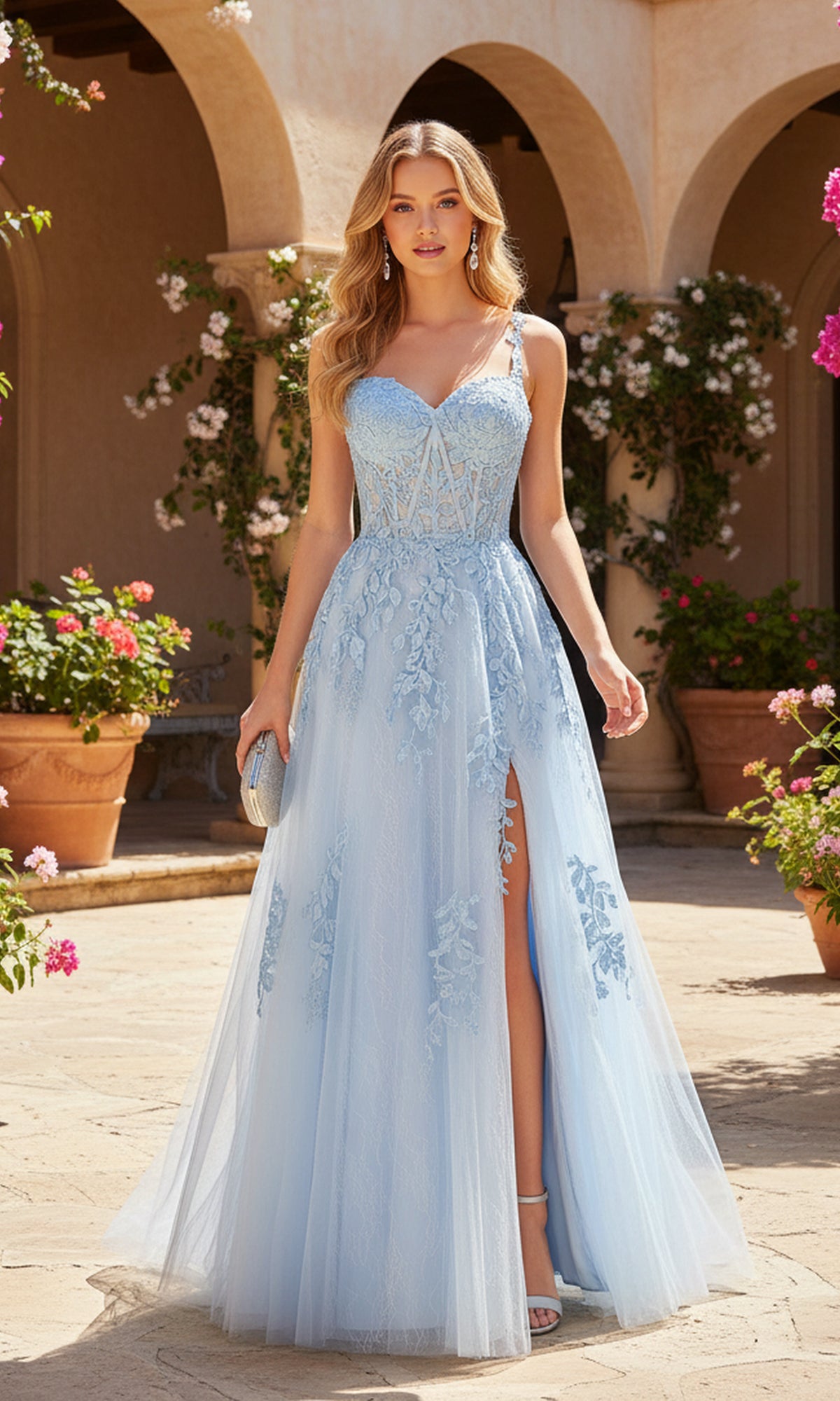A woman in the PromGirl Exclusive 250233, a light blue sleeveless floor-length A-line prom dress with lace appliques and a thigh-high slit, stands outdoors among flowers and potted plants.